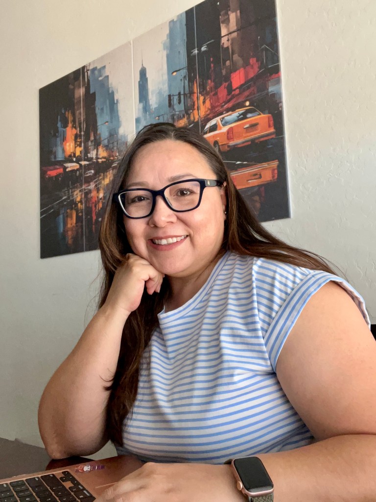 Woman at a table with laptop looking at camera