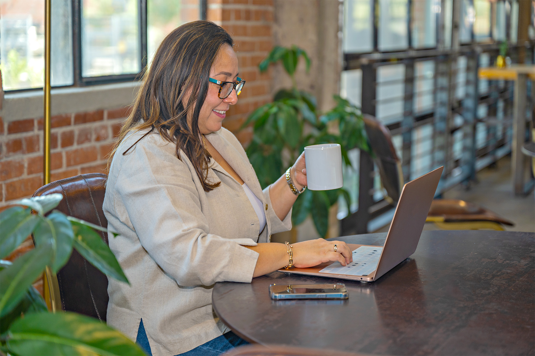 woman with a cup of coffee on one hand typing on laptop with other hand